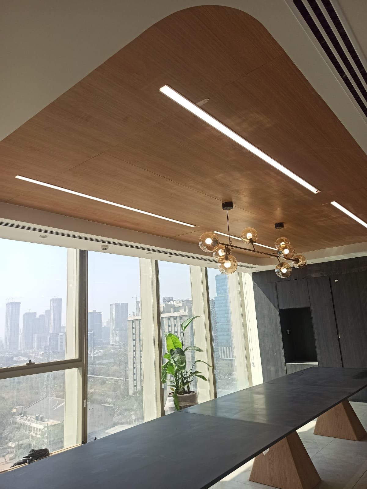Boardroom in Hyderabad with curved micro-perforated wooden ceiling and city skyline through full-height glass.