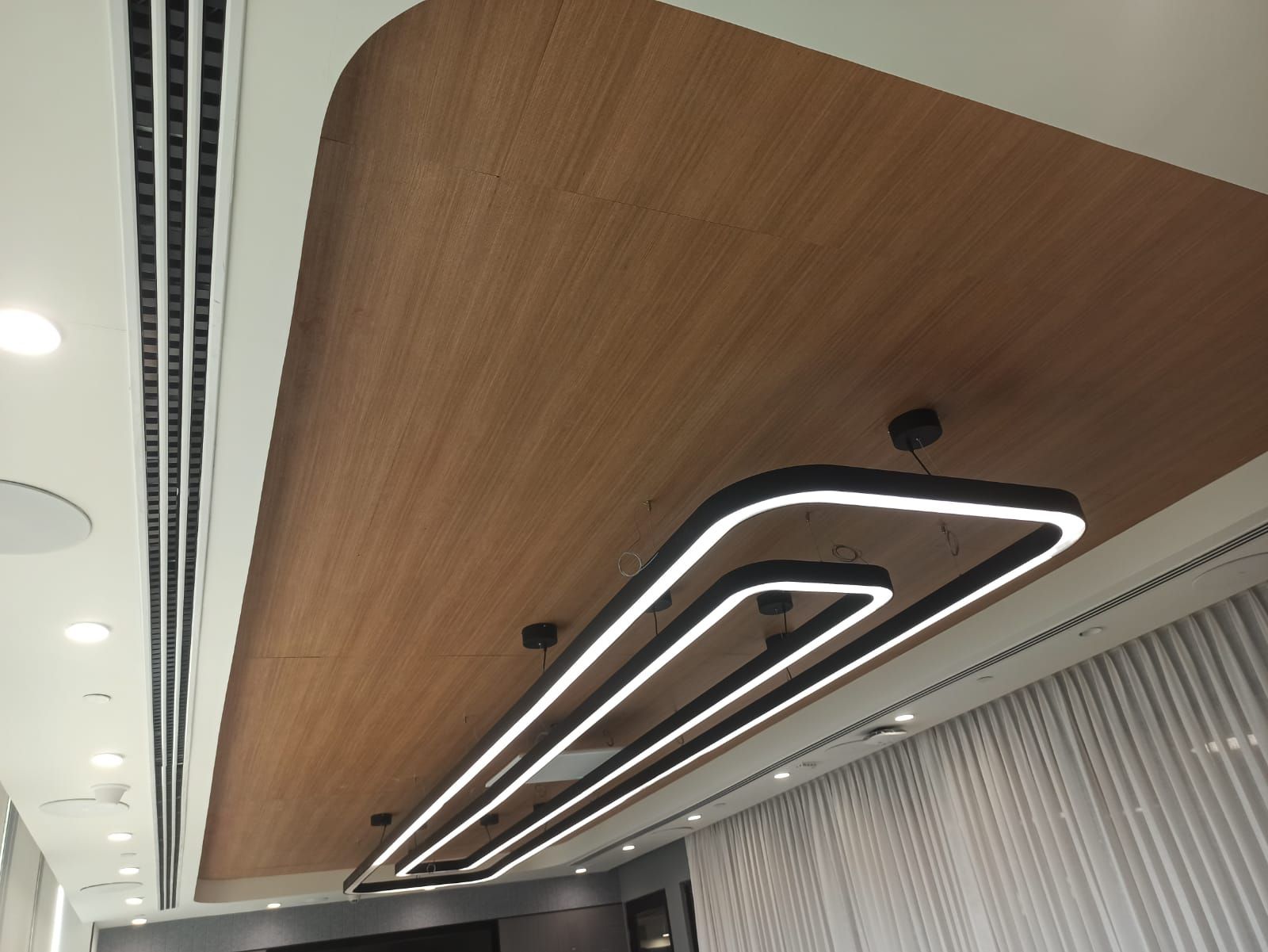 Boardroom angle with rectangular LED pendant below a curved micro-perforated wooden ceiling.